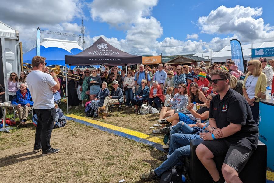  A crowd listens to performers outside under a blue sky