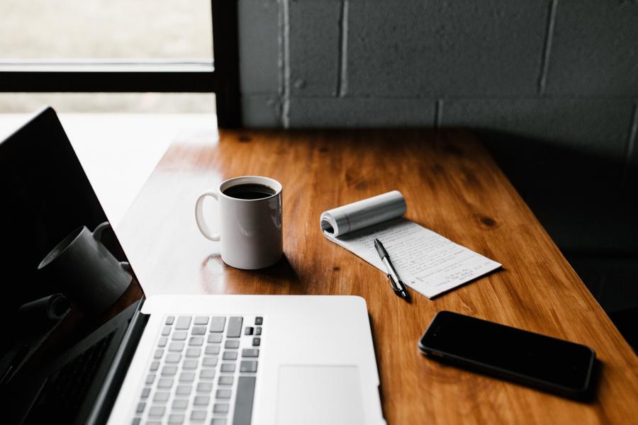 close-up of a laptop, coffee, and notepad on a wooden table