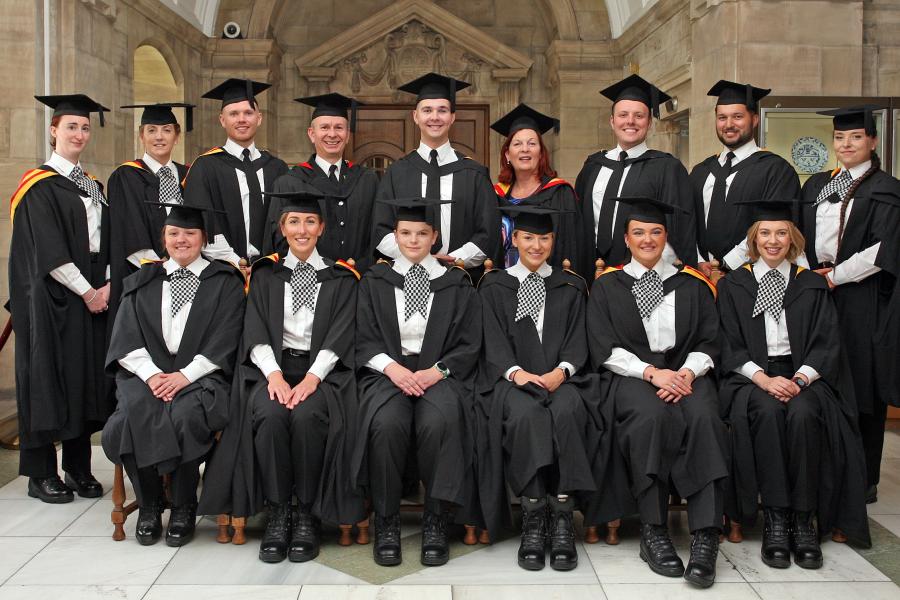  large group of 15 graduates in gowns and mortarboards