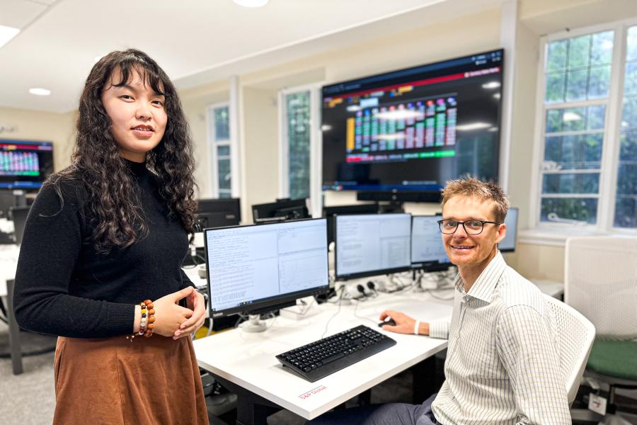 two people standing and sitting in front of computer screens