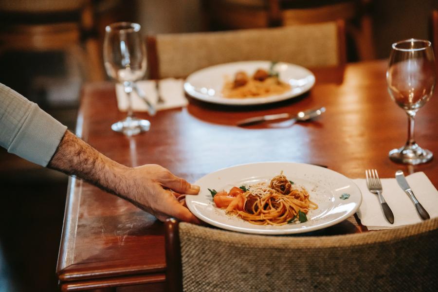 Unrecognizable waiter serving pasta on table with glasses in restaurant