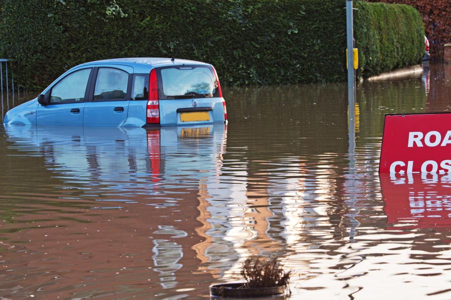  A partly submerged car in a flooded road and a sign saying Road Closed