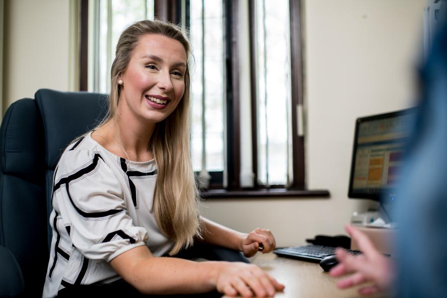 a blonde female medical student sat at a desk in a GP consultation room