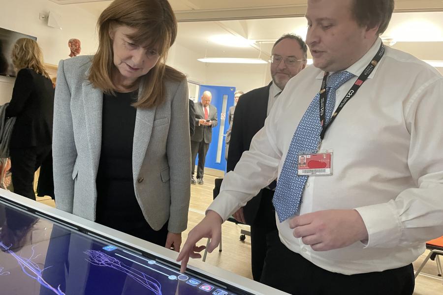 Man in white shirt points at  digital anatomy table with Lesley Griffiths