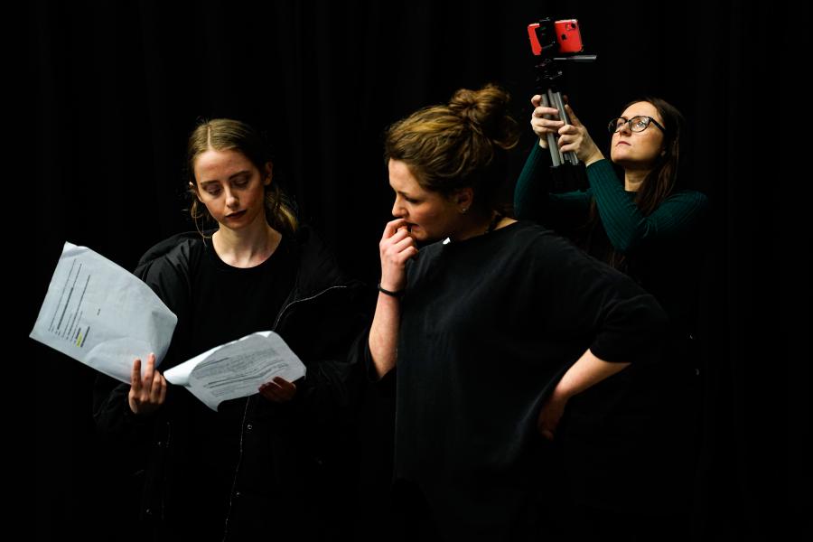 two people looking at sheets of paper directing whilst another is filming behind them 