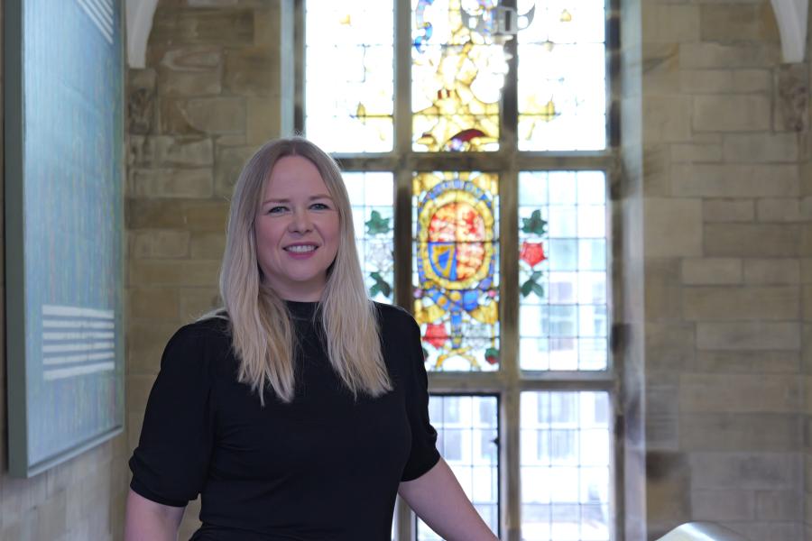 A photograph of Professor Enlli Thomas in front of a stained glass window in the Main Arts Building