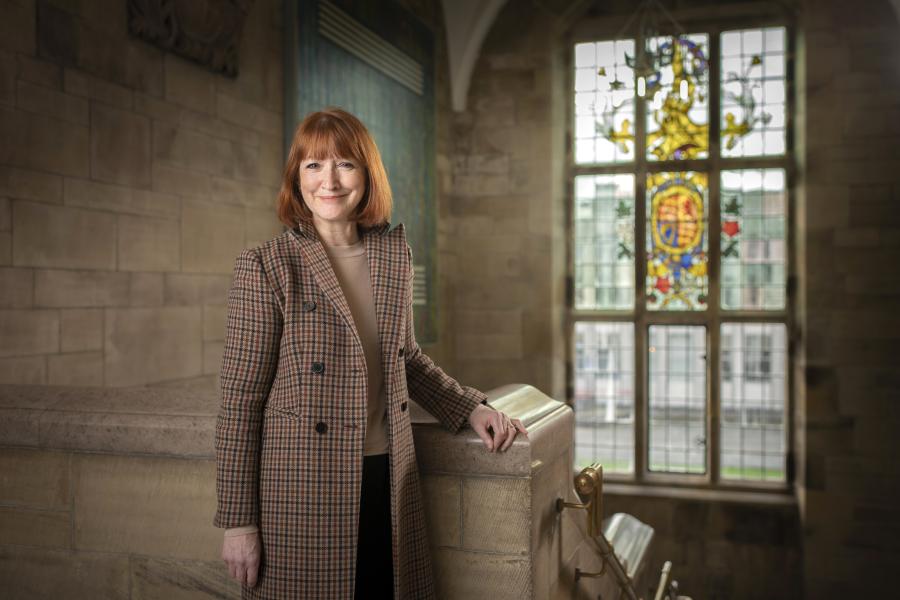 Photo of Marian Wyn Jones in the Profs Corridor in the Main Arts Building, standing in front of a stained glass window