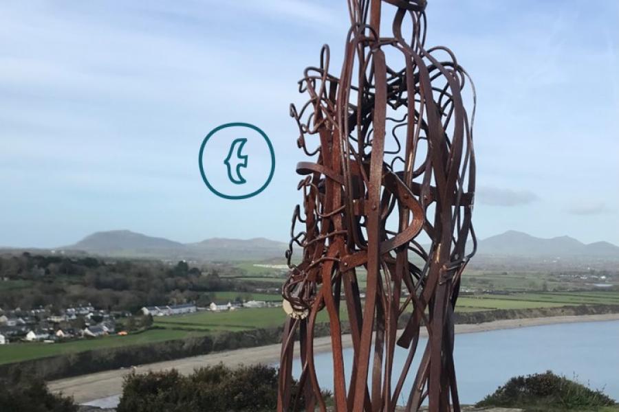 Tin man sculpture sitting against a backdrop of Llyn Peninsula 