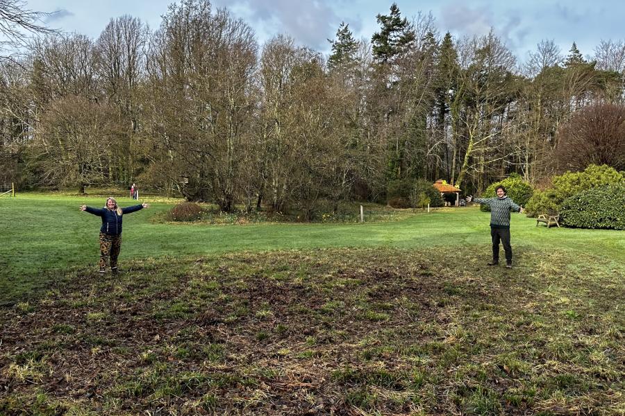 Two people standing on a cleared area with trees in the background