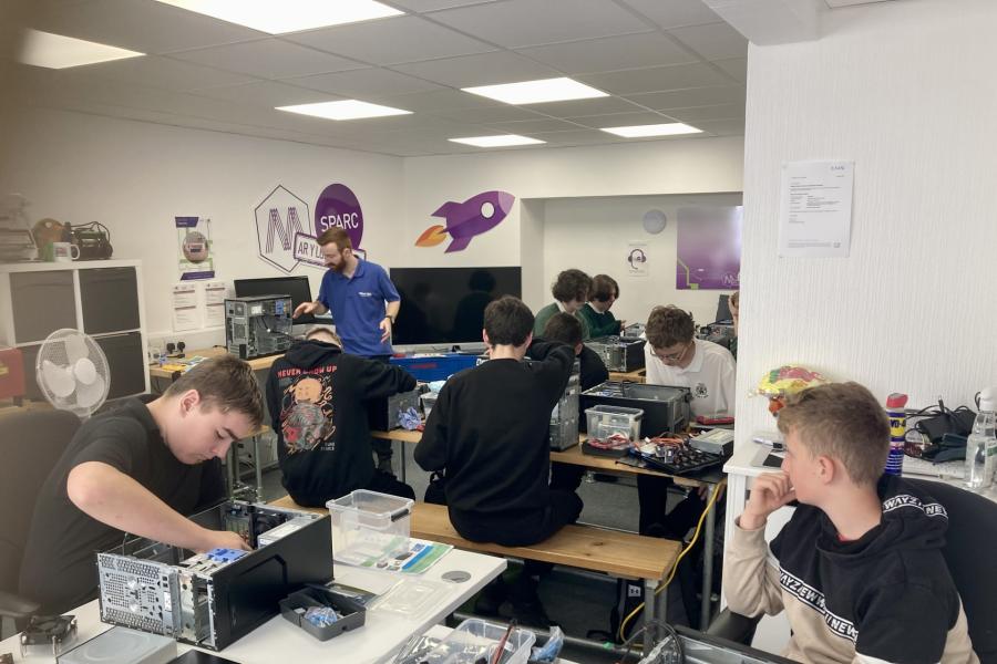 A group of 7 school children following instructions from leader in a computer workshop setting