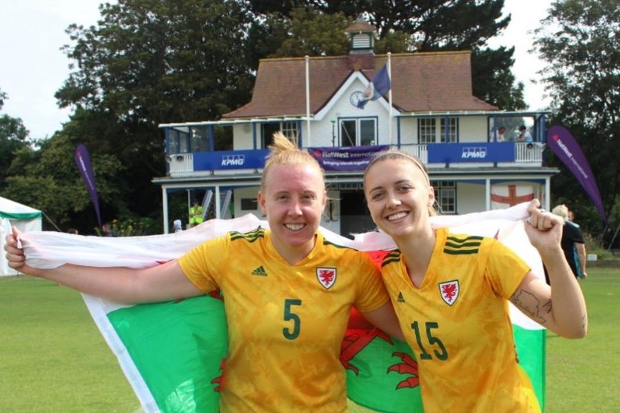 2 female members of staff in their Wales Football Kit flying a Welsh flag following a recent competition 