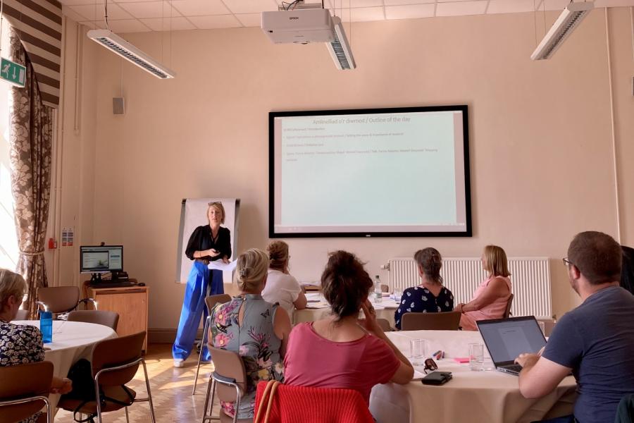 A member of staff presenting at a conference in Neuadd Reichel to a group of (seated) delegates 