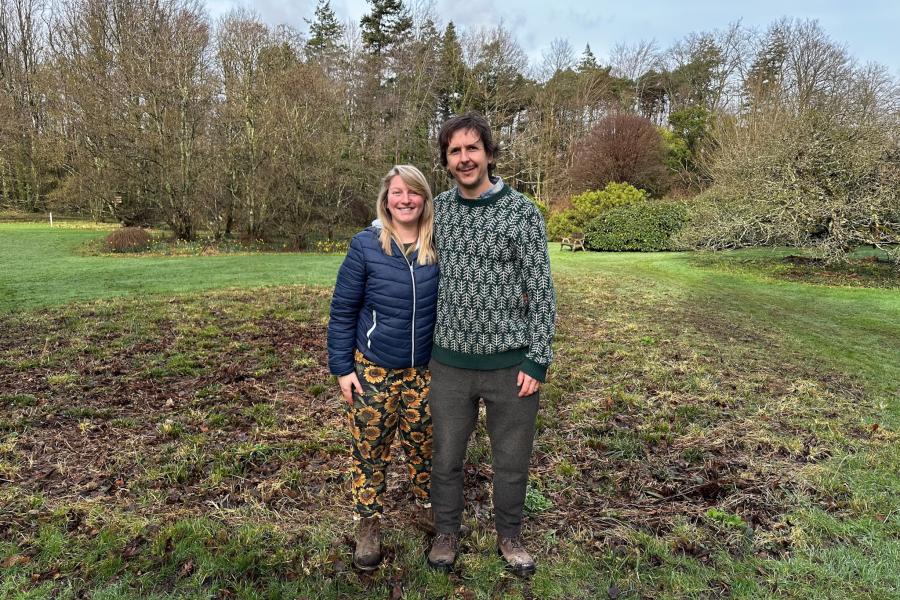 Two people standing in front of a patch of land with trees in the background