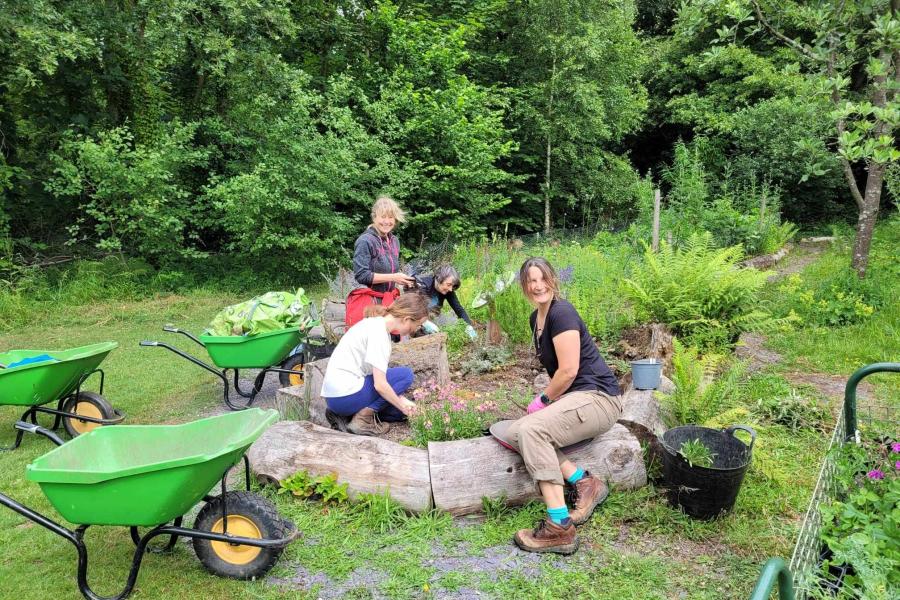 A group of 4 women gardening surrounded by wheel barrows and gardening equipment 