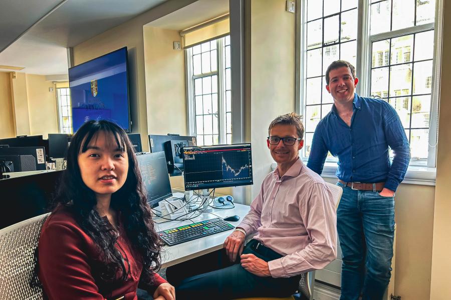 Three people looking at teh camera whilst sitting at a desk showing business data