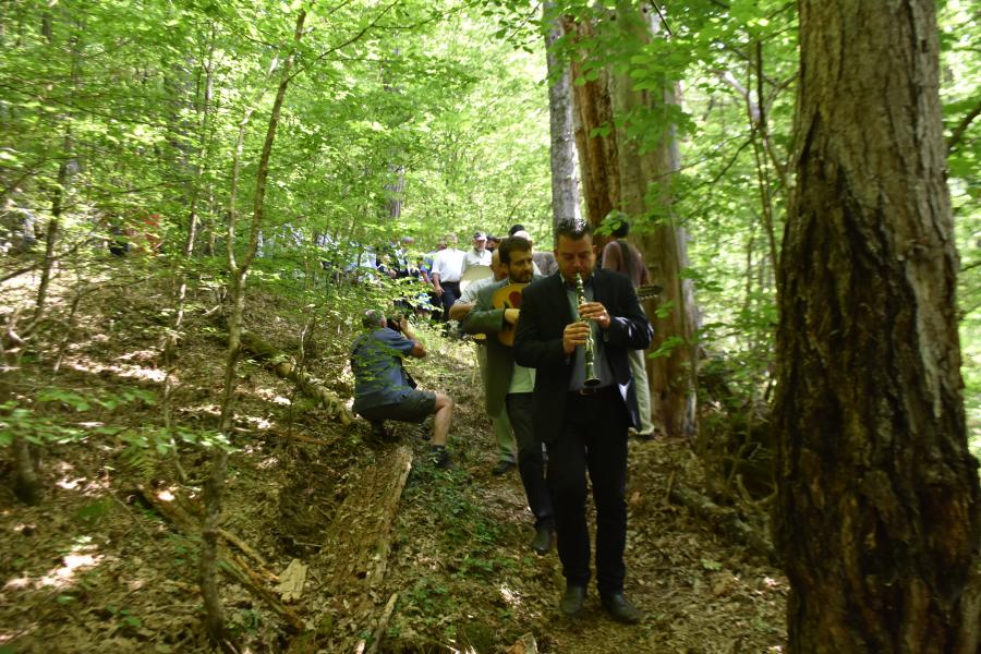 Man paying a wind instrument leads a procession through a forest