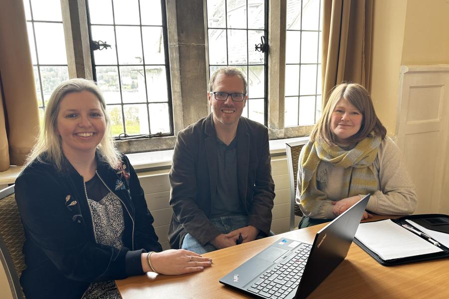 Three people sat at a desk looking at the camera