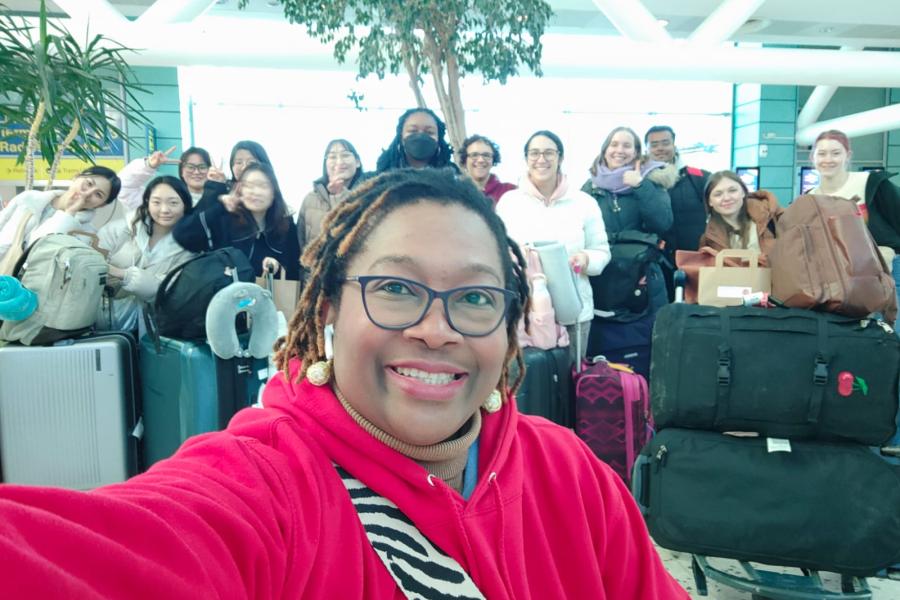 Image of student at an airport with a group of students and suitcases in the background