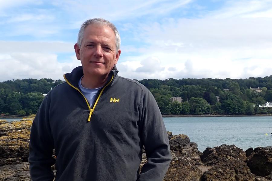 Professor Stuart Jenkins standing on the shore with a forest behind him