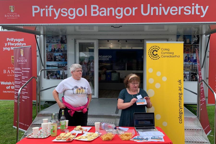 Dau berson yn sefyll o flaen treilar Prifysgol Bangor