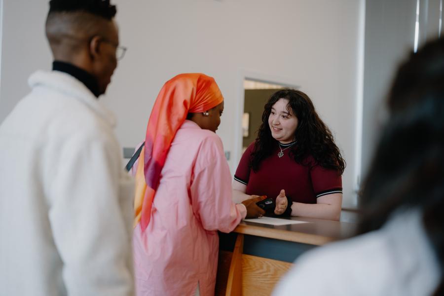 Two students speaking to a member of staff at a reception desk