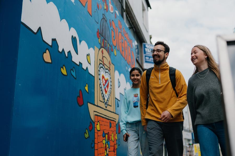 Three students walking in Bangor High Street next to wall mural