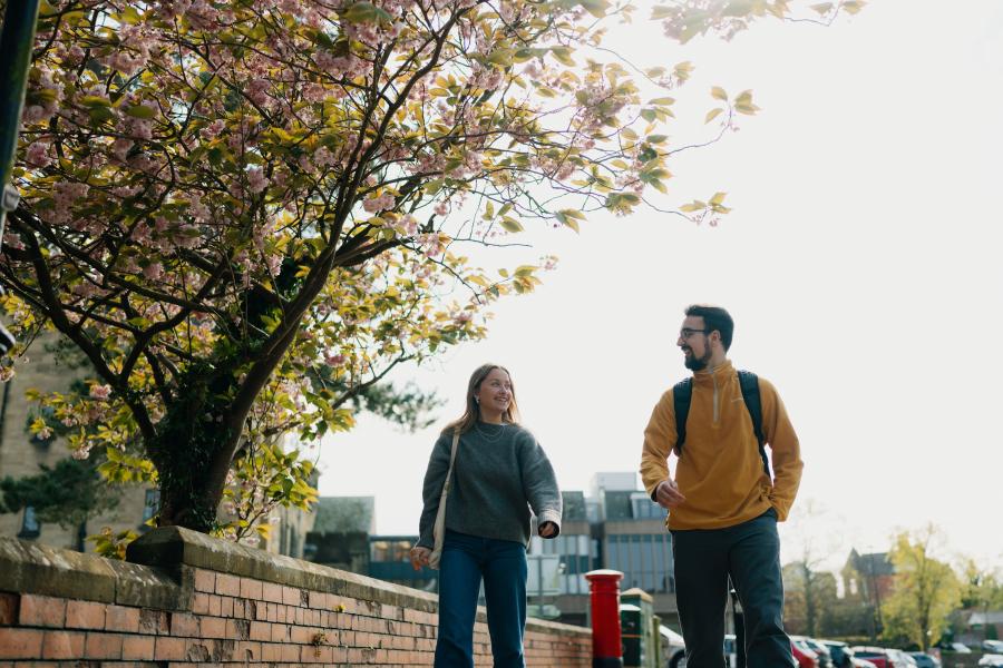 A photo of two students walking down the path outside Main Arts.