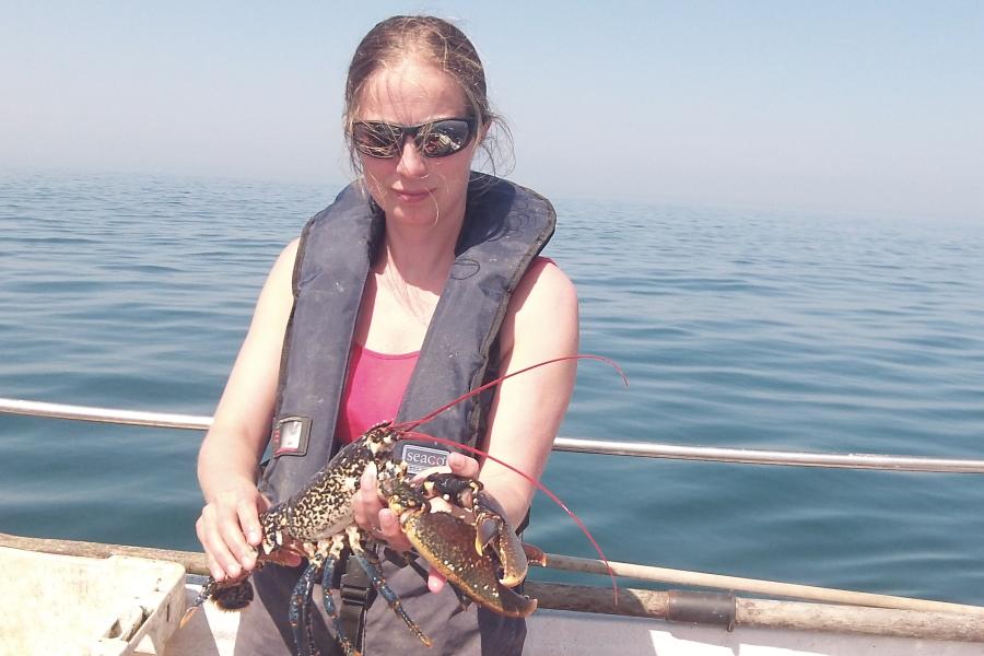 Dr Natalie Hold is holding a lobster whilst on a boat