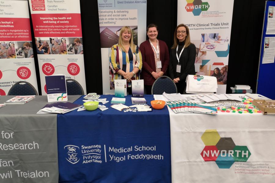 three women standing behind a stall at a research event