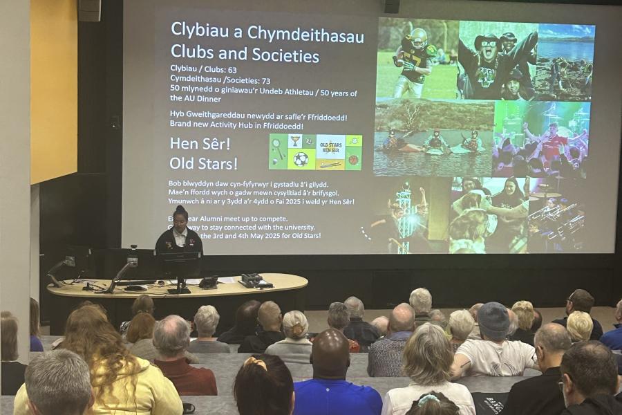 SU President in front of big screen presenting to audience