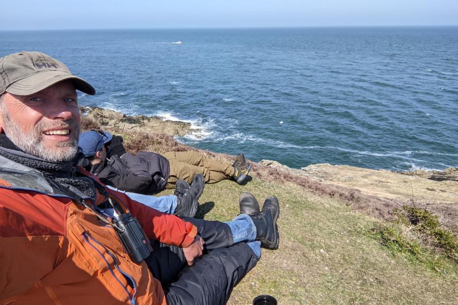 Prof Jan Hiddink sitting on a grassy cliff over looking the ocean