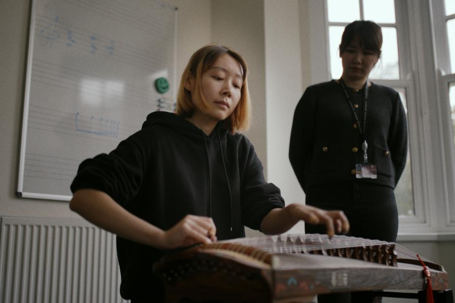 Student playing GuZheng under staff supervision