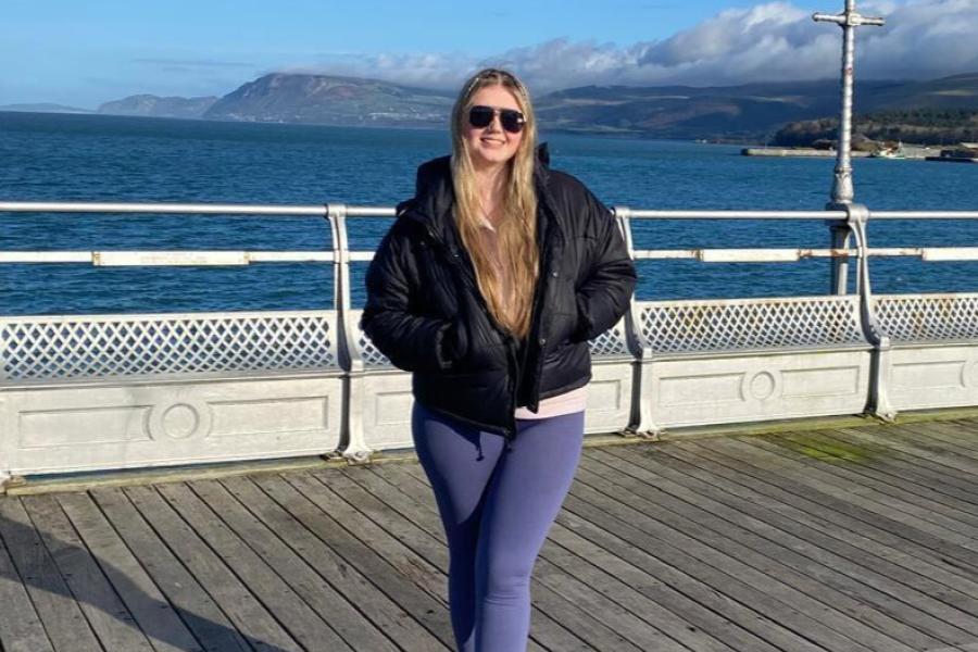 georgia a student is stood on Bangor pier with the sea and mountains in the background