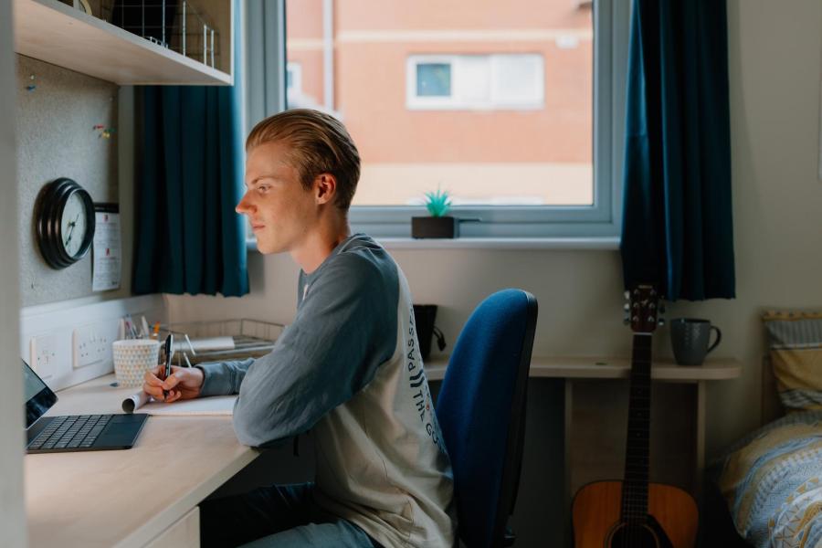 A student working at a desk in a room in halls at Ffriddoedd village