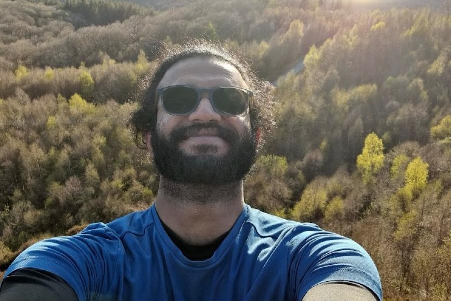 Joe Roy smiling in the sunshine, with a woodland and lake in the background  