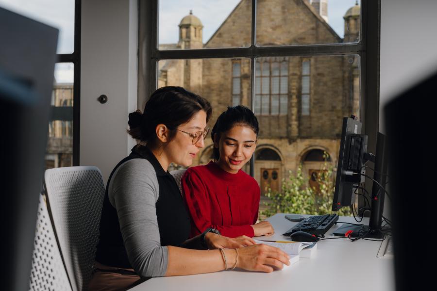 Two students sitting in Richards Reading Room with a view of the Main Arts Building through the window