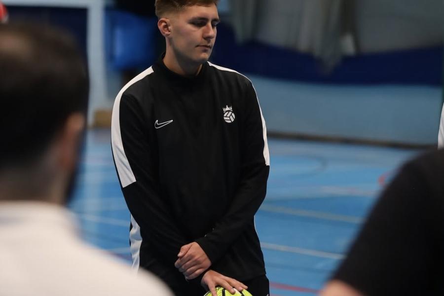 Glenn Swain standing on indoor football pitch in black kit with a yellow football