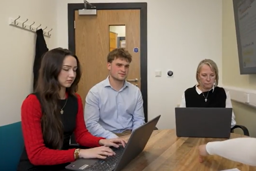 Two students and a lecturer sitting around a table with laptops on the desk chatting to a client in the Legal Advice Clinic.