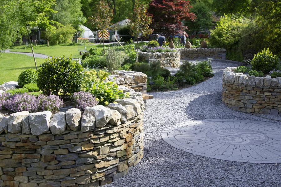 Gravel and paved area with stone-walled circular planters at the Welsh Herbal Garden at Treborth