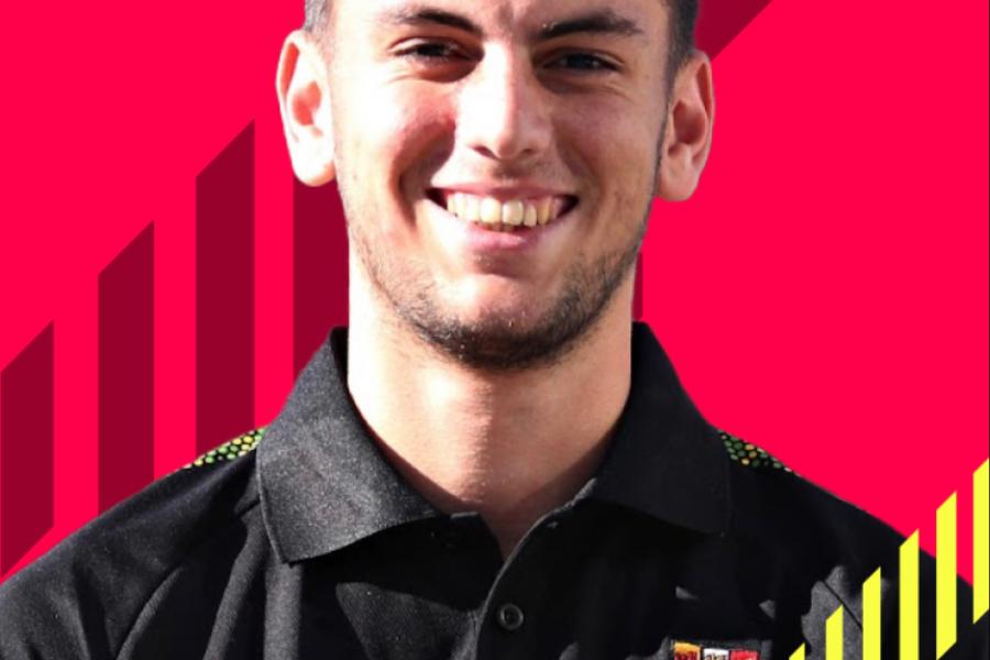 Lewis Thompson looking at camera in Bangor Uni black shirt with red background behind him.