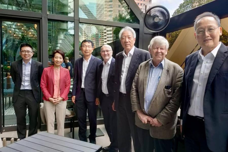Seven people in business attire standing outdoors in a modern urban setting with glass buildings in the background.