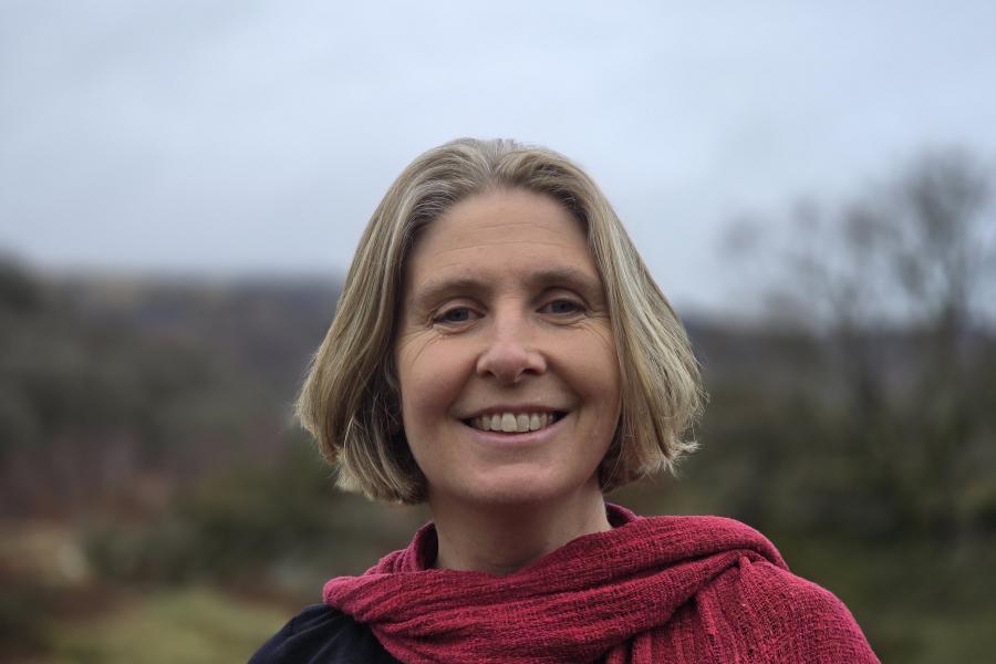 An image of Professor Julia Jones. She has short blonde hair and is standing outdoors wearing a black top and a textured red scarf.