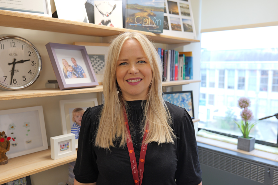 Profile picture of Enlli Thomas smiling in front of a book case full of books
