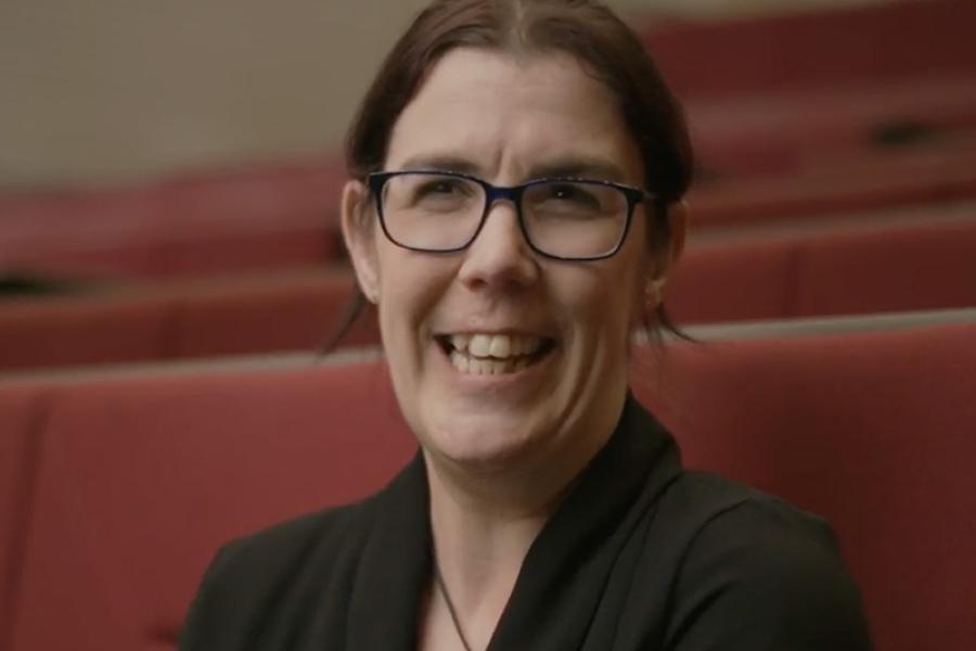 An image of Manon smiling to camera in a large lecture theatre