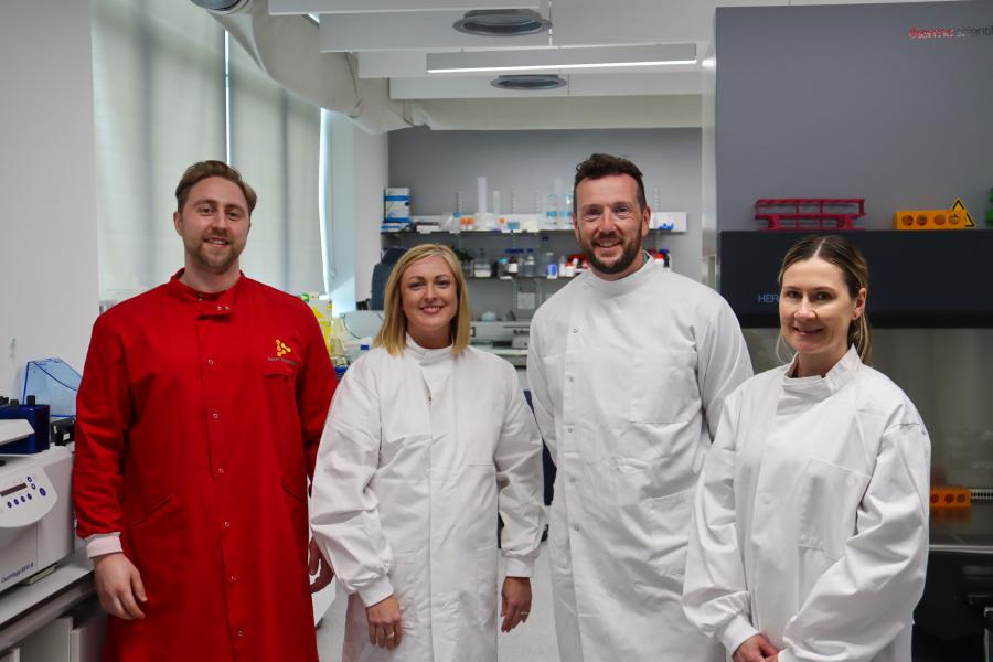 A group of people smiling at the camera wearing lab coats