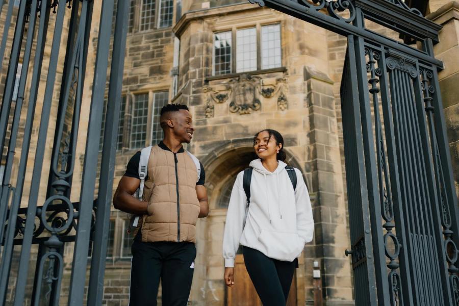 Two students chatting whilst walking through the gate in Main Arts 