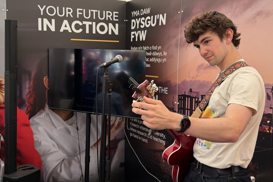 Myfyriwr yn chwarae'r gitar yn ystod yr aduniad