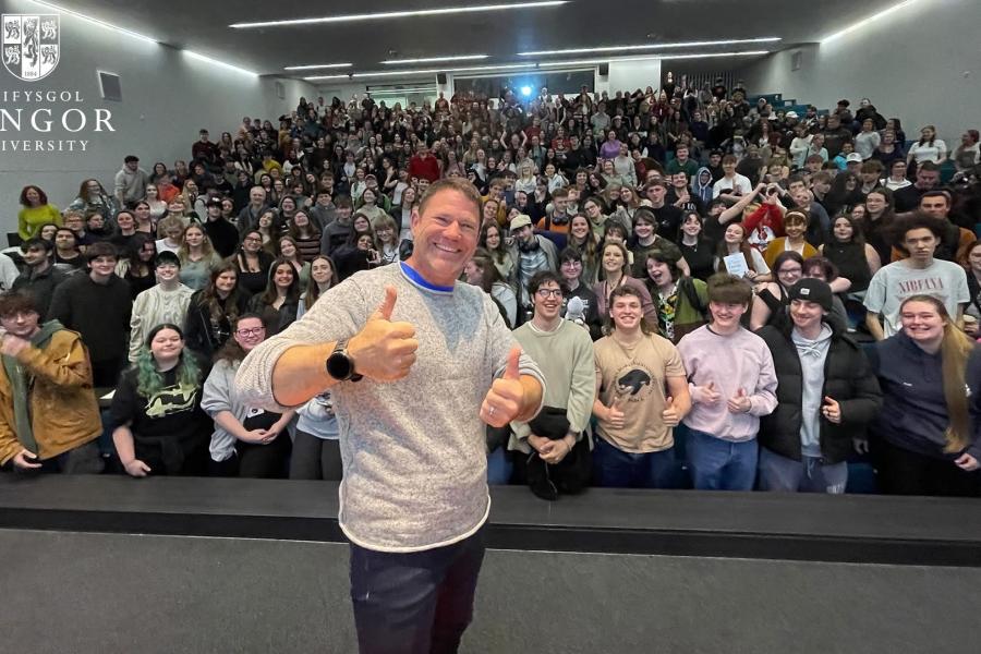 Steve Backshall with thumbs up in front of a lecture theatre full of students 