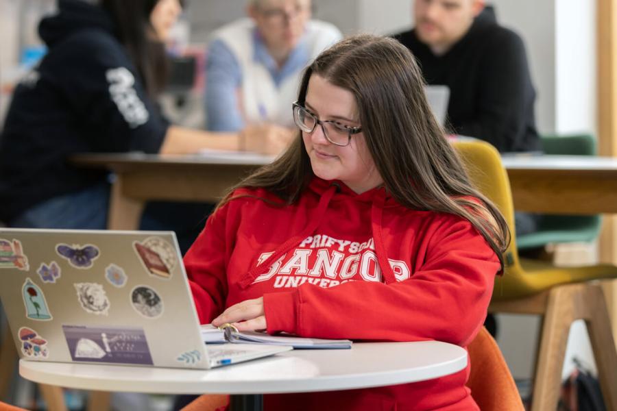 Student working on a computer wearing a red Bangor shirt