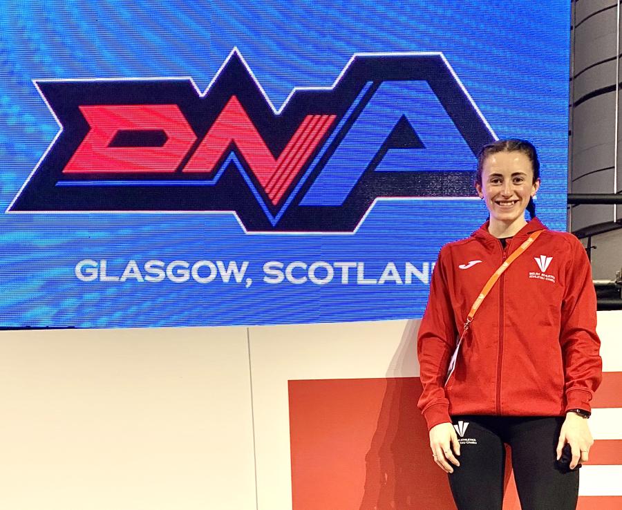 Llun o Ffion Roberts - athletwraig o flaen banner glas gyda'r geiriau DNA Glasgow Scotland